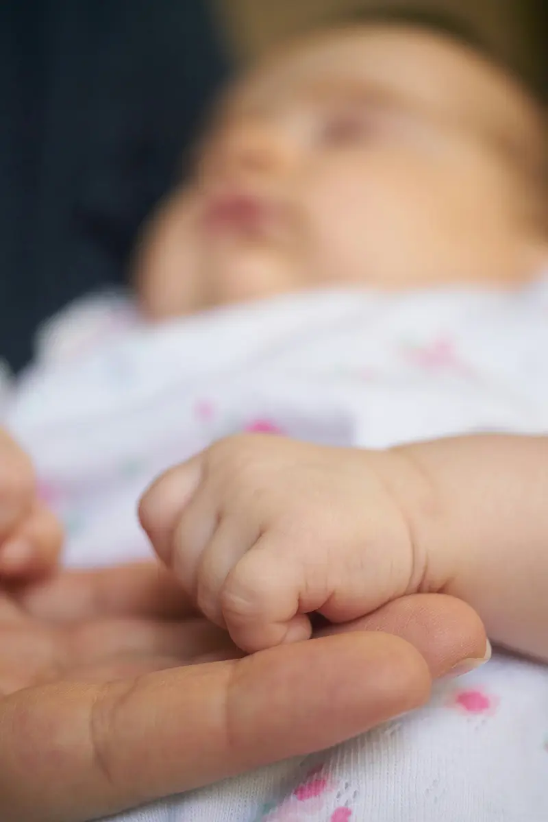 A sleeping baby holding a parent's finger