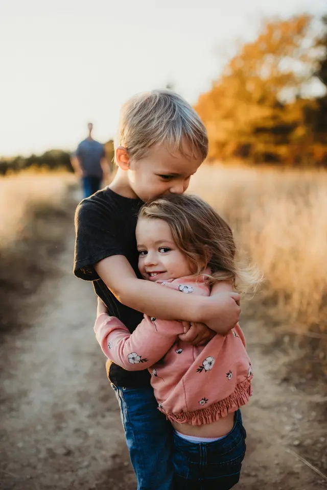 A young boy hugging his little sister outdoors