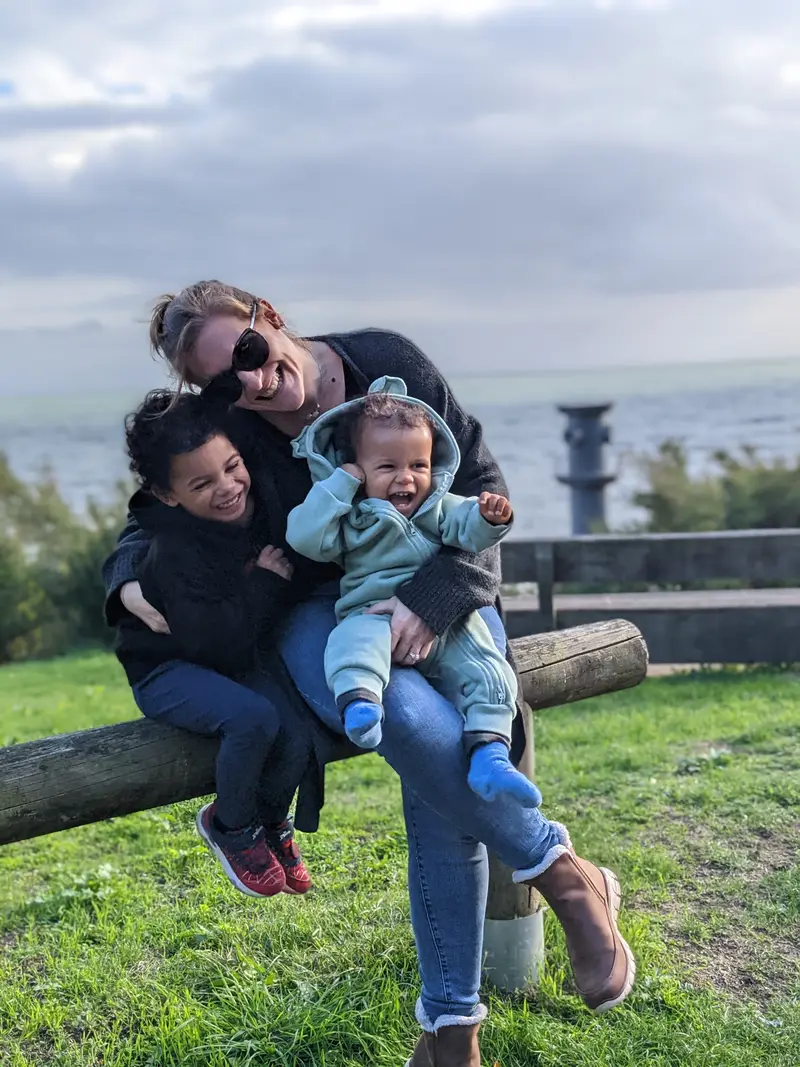 Sylvia outdoors by the sea, hugging two young children